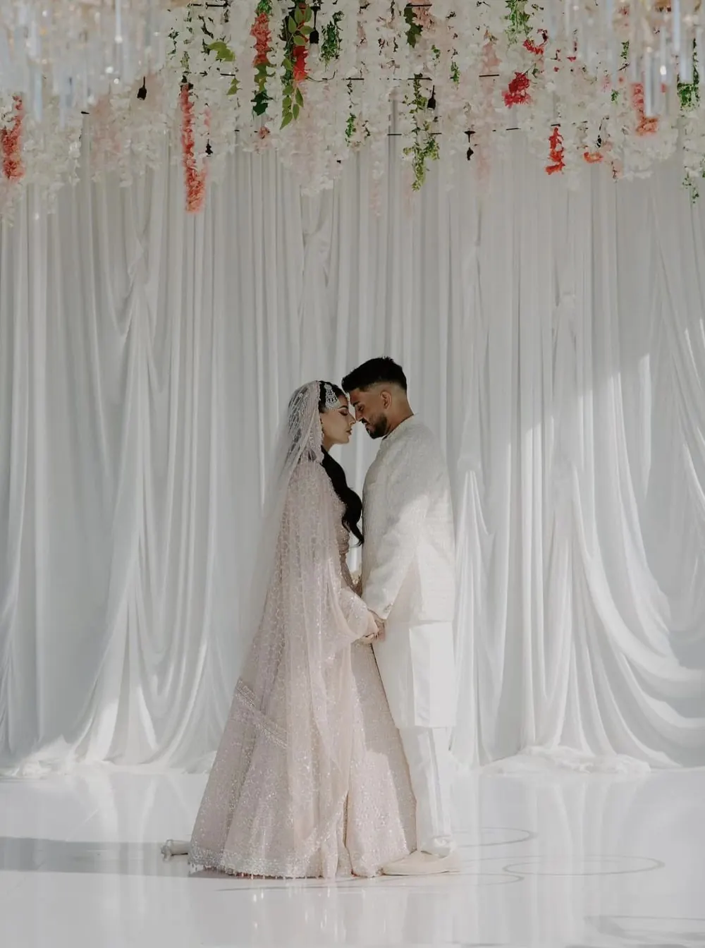 Couple in front of white draped backdrop with hanging florals