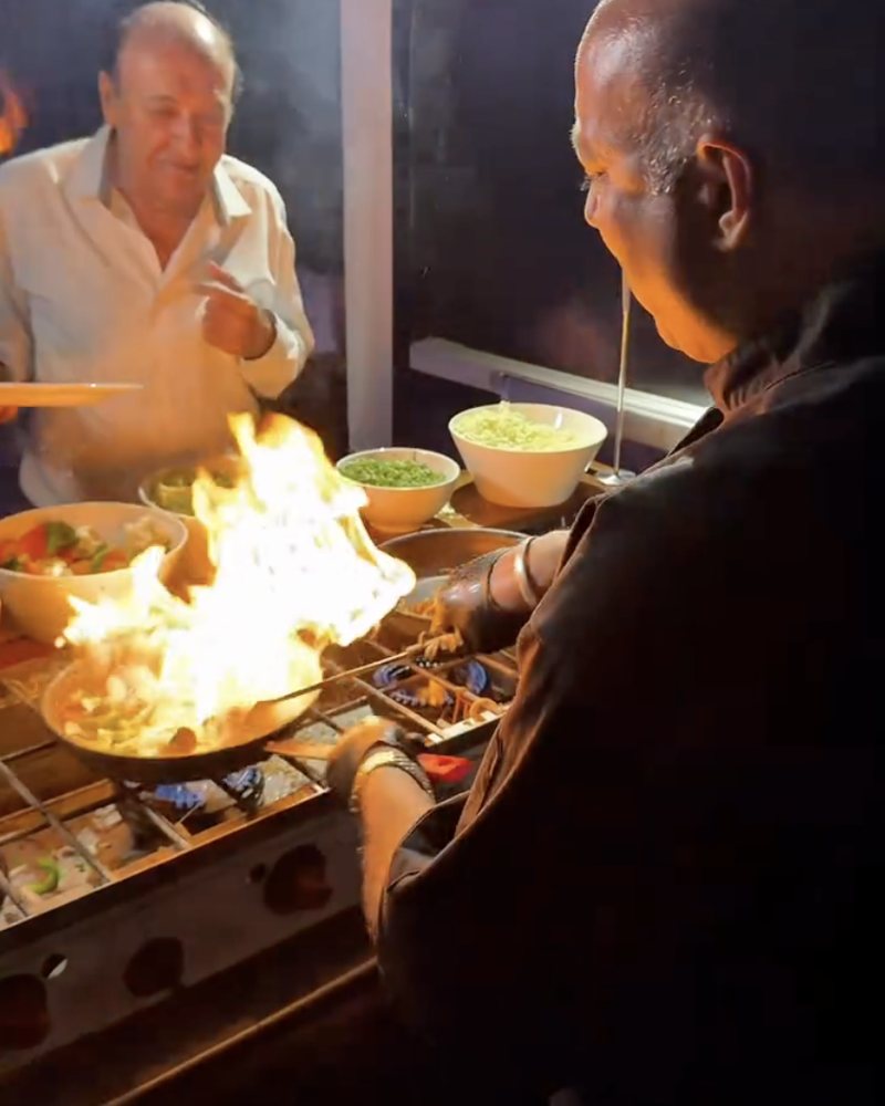 Mantra chefs cooking over an open flame at a live catering station